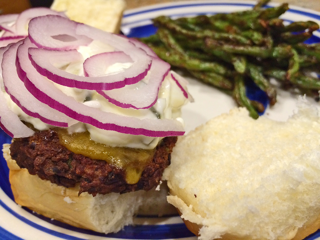 Homemade black bean burgers with cheese, a roll, and red onions.